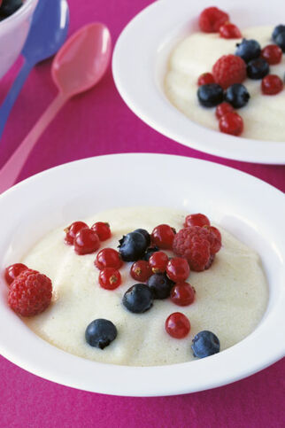 Zwei Schüsseln Grießbrei mit Himbeeren, Blaubeeren und Johannisbeeren auf einem pinken Hintergrund. Grießbrei