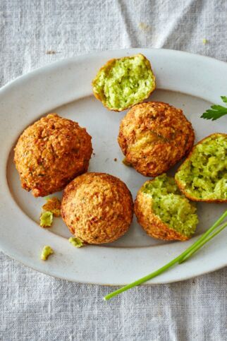 Viel Falafel auf einem Teller mit etwas Koriander. Ein Bällchen ist aufgeschnitten. Im Inneren sind die knusprigen Kichererbsenbällchen grün uns weich. Falafel Kichererbsenbaellchen